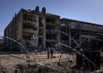 TOPSHOT - People stand beside damaged buildings  at the Vizar company military-industrial complex, after the site was hit by overnight Russian strikes, in the town of Vyshneve, southwestern suburbs of Kyiv, on April 15, 2022. A Ukrainian military factory outside Kyiv that produced missiles allegedly used to hit Russia's Moskva warship was partly destroyed by overnight Russian strikes, an AFP journalist at the scene saw on April 15. A workshop and an administrative building at the Vizar plant were seriously damaged.  (Photo by FADEL SENNA / AFP)