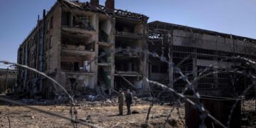 TOPSHOT - People stand beside damaged buildings  at the Vizar company military-industrial complex, after the site was hit by overnight Russian strikes, in the town of Vyshneve, southwestern suburbs of Kyiv, on April 15, 2022. A Ukrainian military factory outside Kyiv that produced missiles allegedly used to hit Russia's Moskva warship was partly destroyed by overnight Russian strikes, an AFP journalist at the scene saw on April 15. A workshop and an administrative building at the Vizar plant were seriously damaged.  (Photo by FADEL SENNA / AFP)